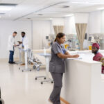 Asian female doctor writing on clipboard at reception desk of hospital ward, copy space. Hospital, medical and healthcare services.